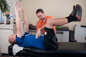 Image: Abdominal Bracing Instruction - Our chiropractor, incorporating conservative sports therapy, guides a male patient in performing a Dead Bug exercise to enhance core strength at Seasons Chiropractic.