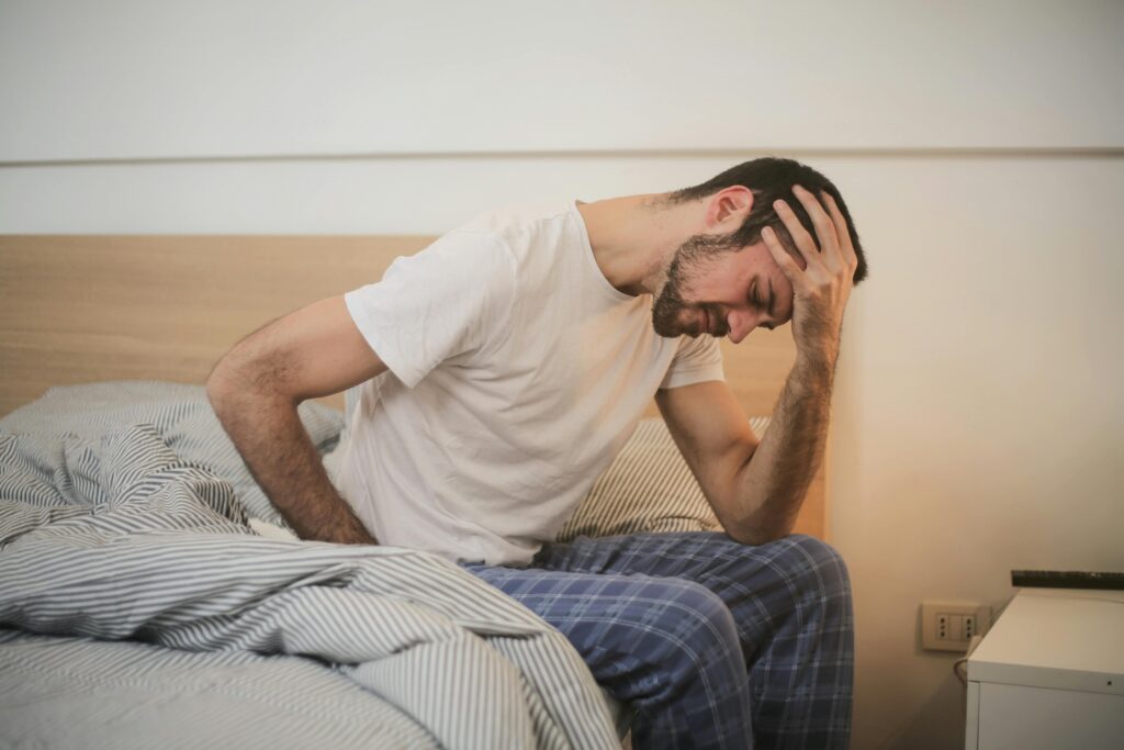 Concussion page: A young man in pajamas holding his head, sitting on a bed, appears to be experiencing a headache.